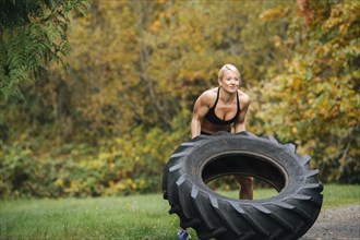 Caucasian woman lifting heavy tire in park