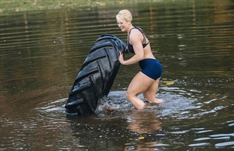 Caucasian woman pushing heavy tire in lake