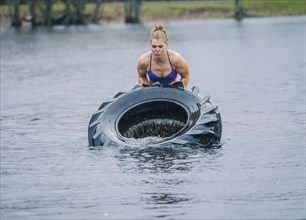 Caucasian woman lifting heavy tire in lake