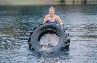 Caucasian woman pushing heavy tire in lake