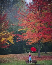 Caucasian woman holding umbrella in rain on park bench
