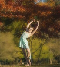 Caucasian ballerina dancing under branches in park
