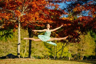 Caucasian ballerina leaping under branches in park