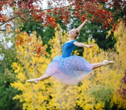 Caucasian ballerina leaping under branches in park