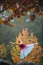 Caucasian ballerina dancing on rock in park