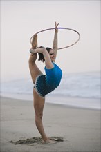 Caucasian gymnast practicing with hoop on beach