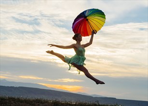 Caucasian ballerina jumping with multicolor umbrella