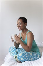 African American woman drinking coffee in bed