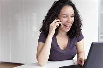 Hispanic woman talking on cell phone and using laptop