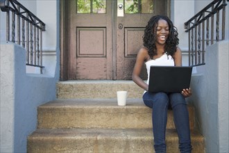 Black woman using laptop on front stoop