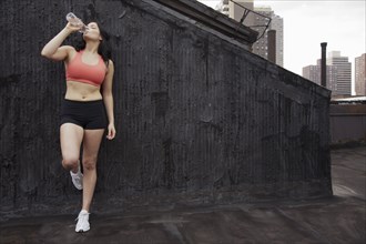 Woman in sportswear drinking water on rooftop