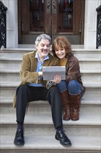 Caucasian couple using digital tablet on front stoop