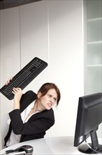 Frustrated businesswoman about to hit computer with keyboard
