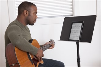 Black man practicing guitar with digital tablet
