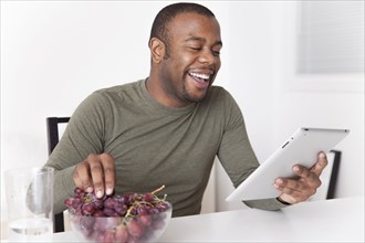 Black man eating grapes and using digital tablet