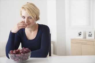 Caucasian woman eating grapes in kitchen
