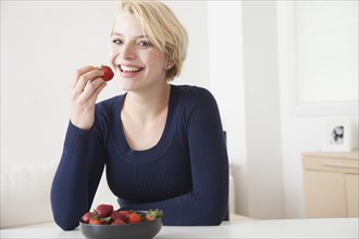 Caucasian woman eating strawberries in kitchen