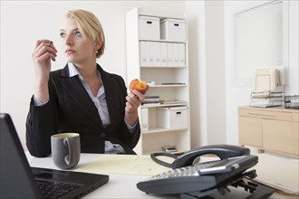 Caucasian businesswoman eating at desk in office