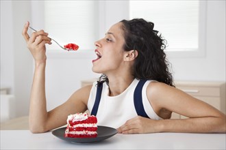Hispanic woman eating cake in kitchen