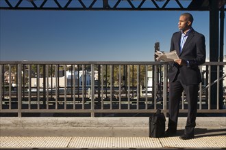 Black businessman reading newspaper and waiting at train station