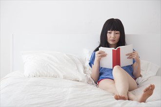 Chinese woman reading book on bed