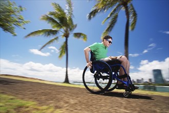 Disabled man racing in wheelchair by urban beach