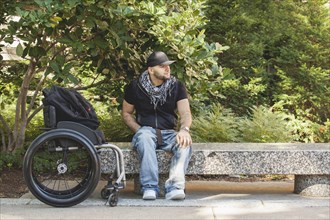 Disabled man and wheelchair sitting on stone bench