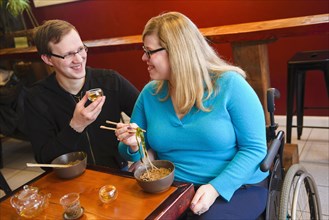 Paraplegic woman and boyfriend eating noodles in tea shop