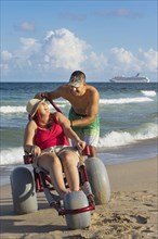 Man pushing paraplegic girlfriend in wheelchair on beach