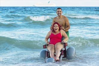 Man pushing paraplegic girlfriend in wheelchair on beach