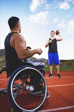 Paraplegic athlete in wheelchair tossing ball with friend