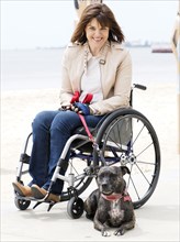 Woman sitting in wheelchair at waterfront with dog on leash