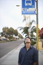 Mixed race man looking at bus stop sign