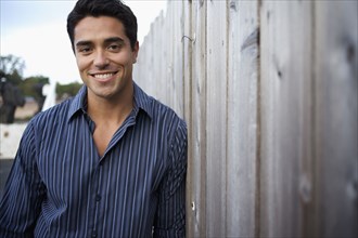 Mixed race man leaning against fence