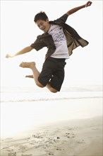 Mixed race boy jumping on beach