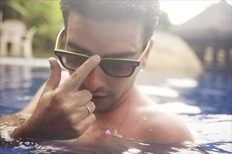 Mixed race man adjusting sunglasses in swimming pool