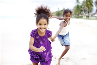 Mixed race sisters holding hands running on beach