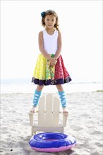 Mixed race girl standing on chair on beach