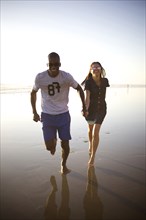 Happy couple holding hands and running on beach
