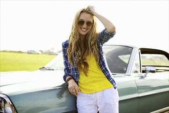 Smiling Caucasian woman leaning against car