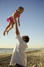 Father lifting daughter in air on beach