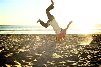 Father and daughter doing cartwheels on beach