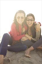 Smiling mixed race sisters sitting on beach
