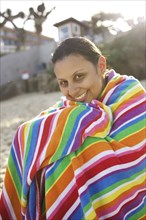 Mixed race woman sitting on beach wrapped in towel