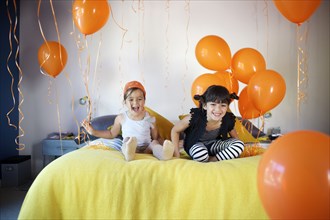 Girls sitting on bed together with balloons