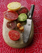 Various juicy sliced tomatoes on cutting board with knife