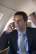Hispanic businessman using cell phone on airplane