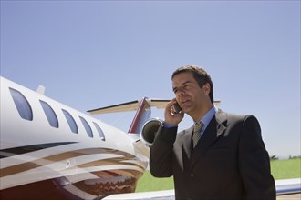 Hispanic businessman using cell phone next to private jet