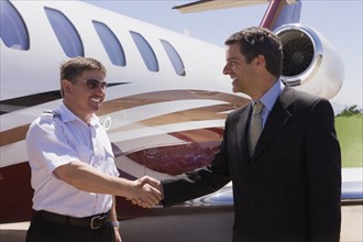 Businessman and pilot shaking hands outside private jet