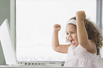 Hispanic girl cheering and using laptop